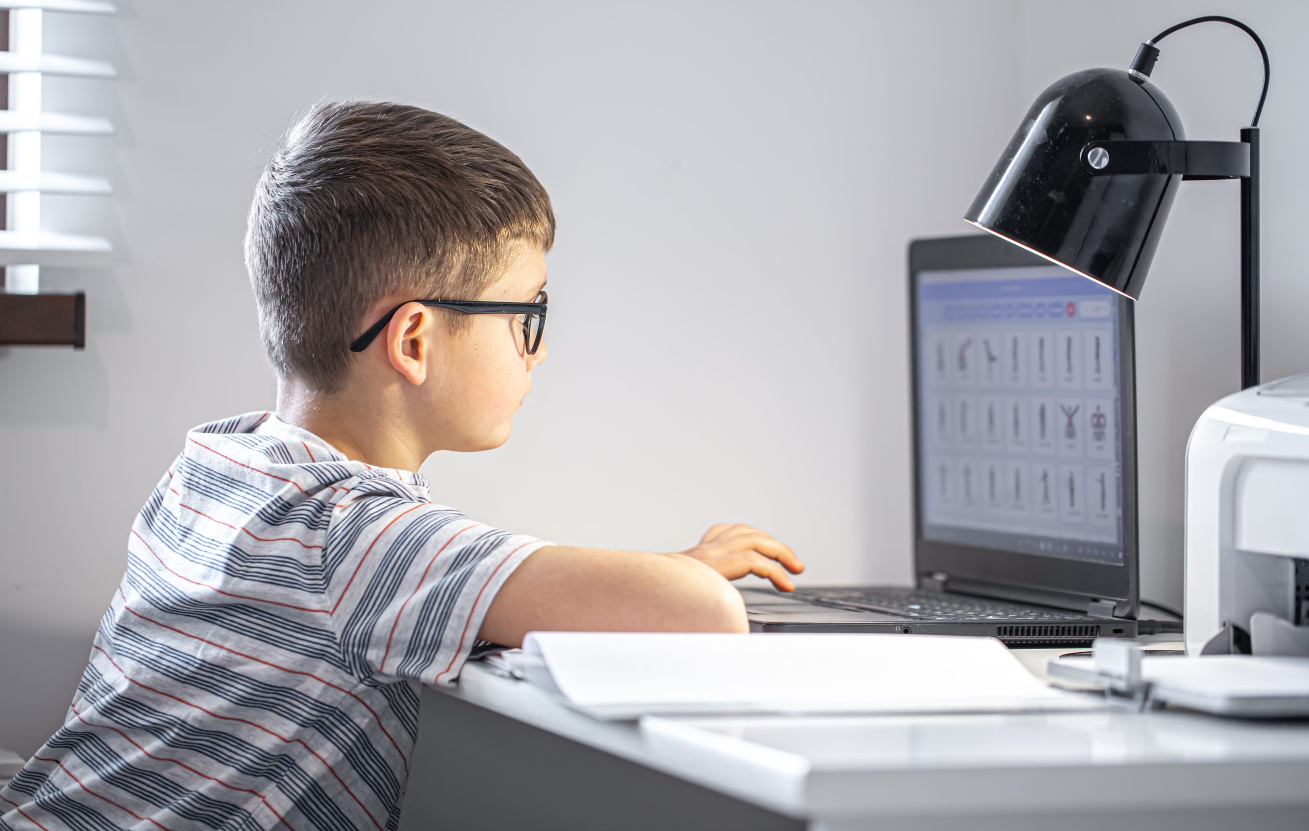elementary school student with glasses sits table with laptop does his homework online scaled